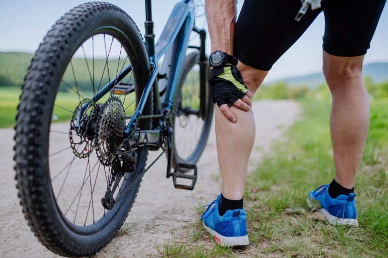 Close-up of active senior man in sportswear suffiering from pain in his knee after cycling, in park in summer - Human Integrated Performance